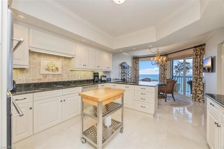 Kitchen with a peninsula, crown molding, a chandelier, backsplash, and a raised ceiling