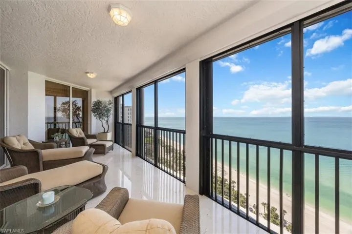 Sunroom featuring expansive windows, view of water and beach, and a textured ceiling