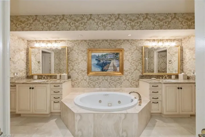 Full bath featuring wallpapered walls, a tub with jets, two vanities, and light tile patterned flooring