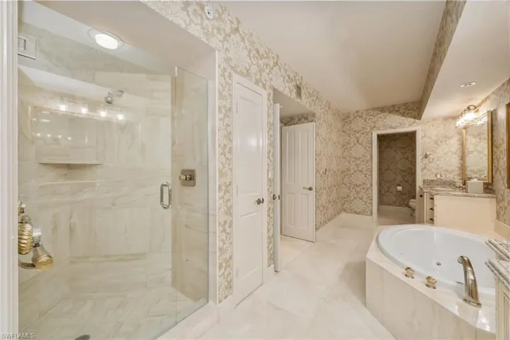 Full bath featuring vanity, a jetted tub, wallpapered walls, and a marble finish shower