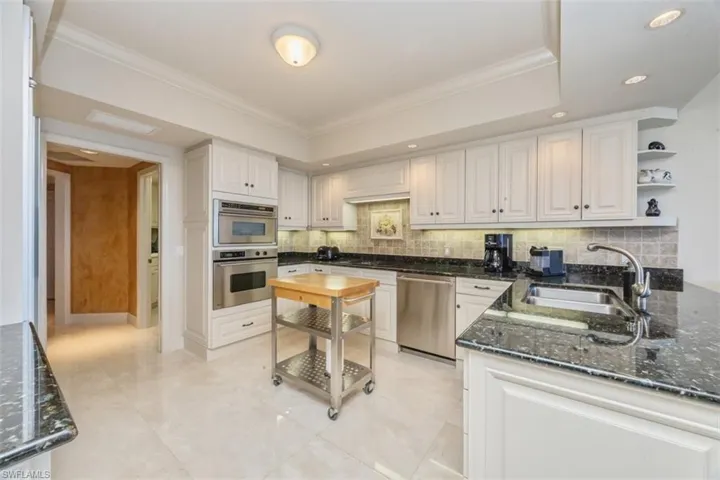 Kitchen with dark stone countertops, open shelves, white cabinetry, appliances with stainless steel finishes, and crown molding