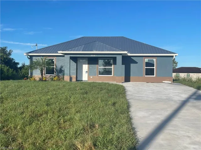 View of front of property with a front yard, stucco siding, a standing seam roof, a metal roof, and driveway