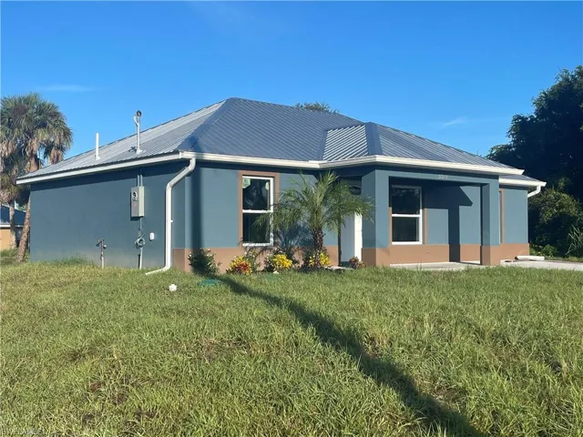 Rear view of property featuring stucco siding, a yard, and a metal roof