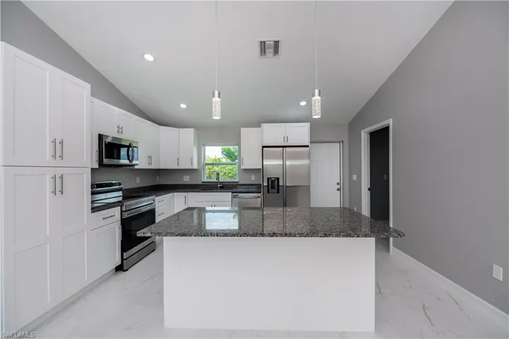 Kitchen featuring appliances with stainless steel finishes, lofted ceiling, a center island, pendant lighting, and dark stone countertops