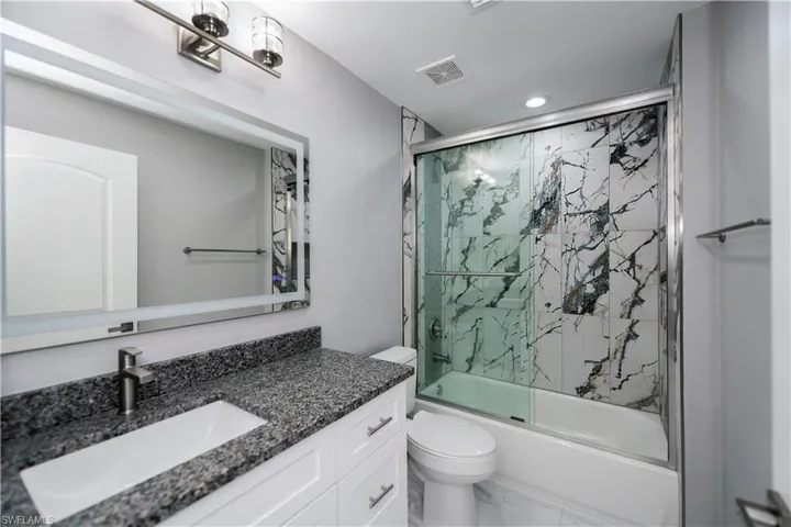 Full bath featuring enclosed tub / shower combo, vanity, marble look tiles, and recessed lighting