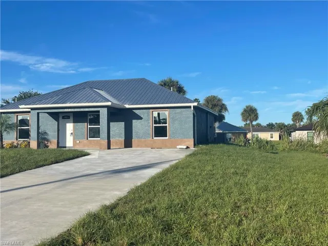 View of front facade featuring a front yard, stucco siding, concrete driveway, and a metal roof