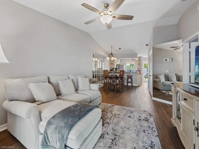 Living area featuring ceiling fan with notable chandelier, baseboards, dark wood finished floors, and vaulted ceiling
