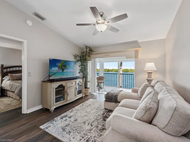 Living room featuring dark wood-type flooring, visible vents, vaulted ceiling, and a ceiling fan