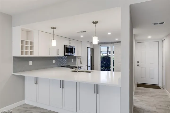Kitchen with appliances with stainless steel finishes, kitchen peninsula, hanging light fixtures, and white cabinets