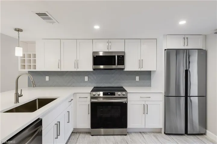 Kitchen featuring white cabinetry, appliances with stainless steel finishes, decorative backsplash, pendant lighting, and sink