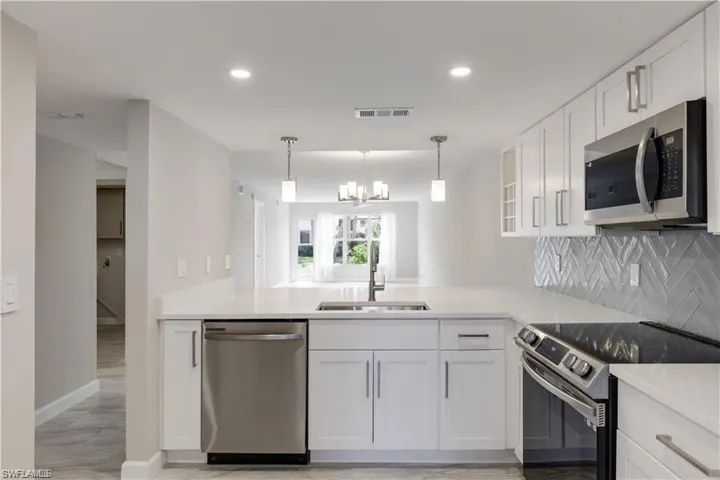 Kitchen featuring appliances with stainless steel finishes, light hardwood / wood-style flooring, white cabinets, sink, and backsplash