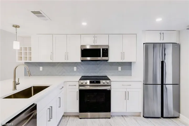 Kitchen with appliances with stainless steel finishes, tasteful backsplash, white cabinets, sink, and pendant lighting