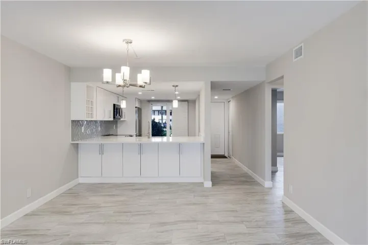 Kitchen featuring stainless steel appliances, pendant lighting, kitchen peninsula, backsplash, and white cabinetry