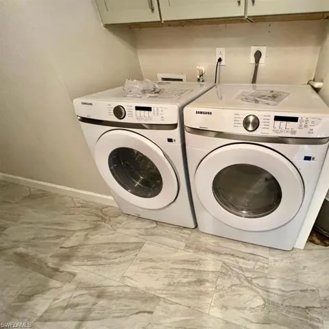 Clothes washing area featuring light tile patterned flooring, washer and dryer, and cabinets