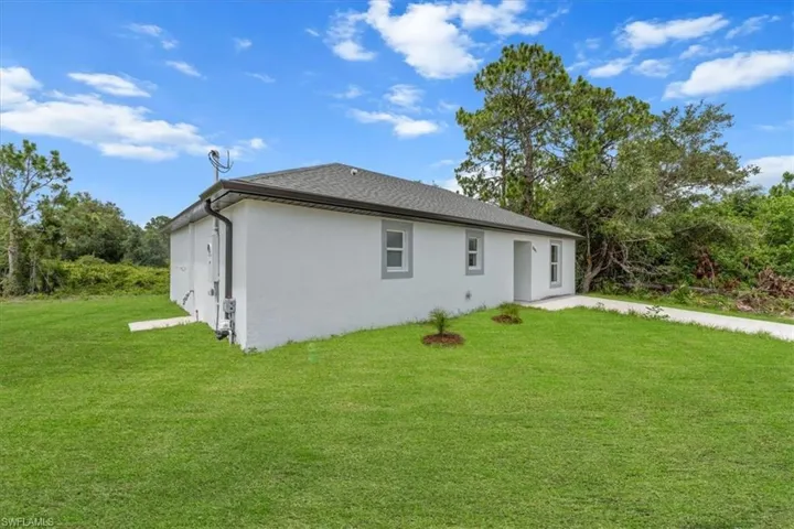 Back of house featuring stucco siding, a yard, and roof with shingles