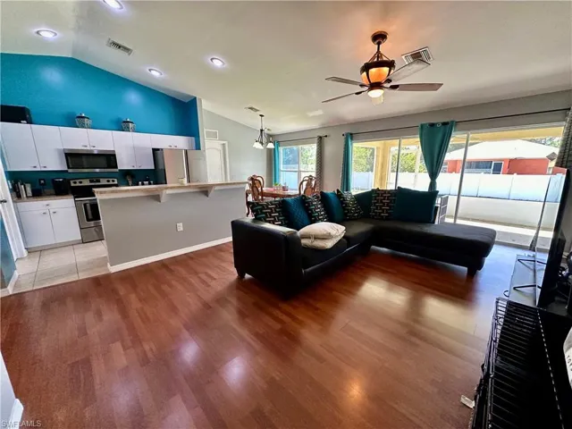 Living room with ceiling fan with notable chandelier, light hardwood / wood-style flooring, and lofted ceiling