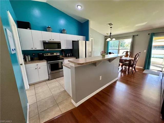 Kitchen with pendant lighting, appliances with stainless steel finishes, light wood-type flooring, and white cabinetry