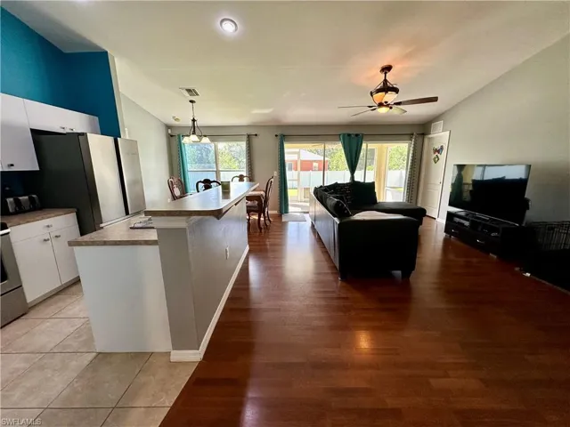 Kitchen featuring light hardwood / wood-style floors, a kitchen island with sink, ceiling fan, pendant lighting, and white cabinets