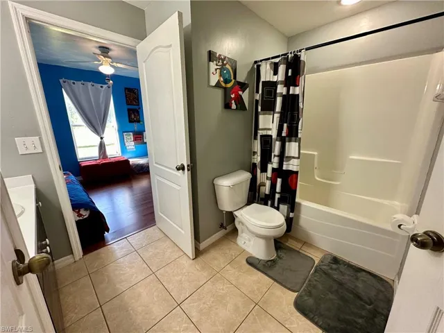 Full bathroom featuring ceiling fan, vanity, shower / bathtub combination with curtain, tile patterned floors, and toilet