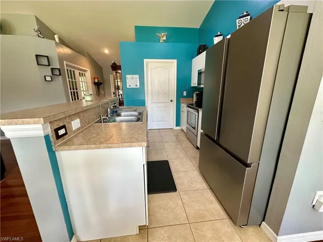 Kitchen featuring sink, stainless steel appliances, kitchen peninsula, lofted ceiling, and light tile patterned floors