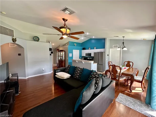 Living room with ceiling fan with notable chandelier, dark hardwood / wood-style floors, and vaulted ceiling