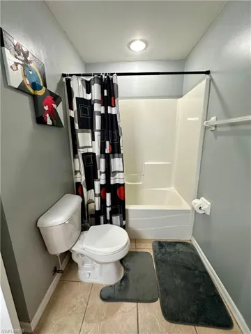 Bathroom with shower / bath combo with shower curtain, tile patterned floors, and toilet