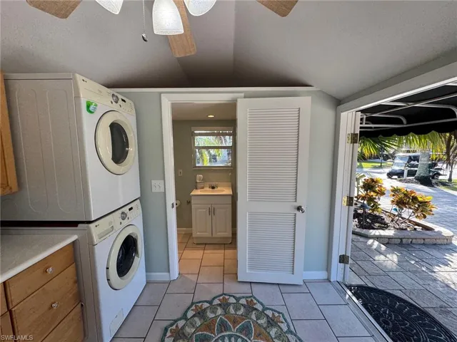 Washroom with a textured ceiling, stacked washer / drying machine, light tile patterned floors, and sink