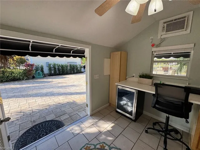 Office space with a wall mounted air conditioner, vaulted ceiling, beverage cooler, ceiling fan, and light tile patterned floors