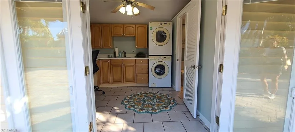 Clothes washing area with ceiling fan, sink, cabinets, light tile patterned floors, and stacked washer and clothes dryer