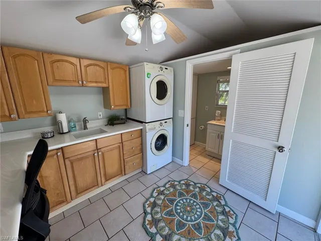 Washroom featuring ceiling fan, sink, cabinets, stacked washing maching and dryer, and light tile patterned floors