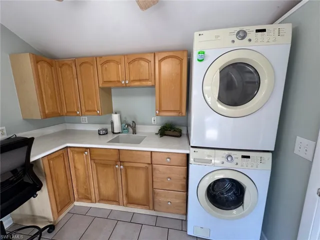 Laundry area with cabinets, light tile patterned floors, stacked washer / dryer, and sink