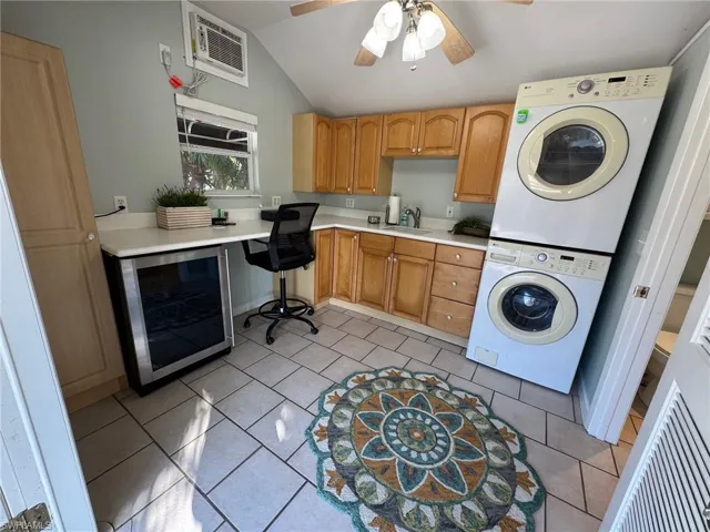 Washroom featuring ceiling fan, sink, beverage cooler, stacked washer / dryer, and light tile patterned floors