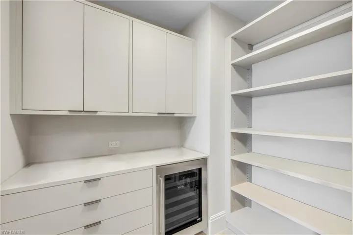 A sizable double pantry with integrated wine cooler and custom drawer storage. There is an adjoining large room with extra storage space.