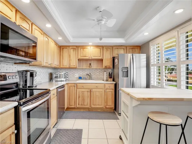 Kitchen with stainless steel appliances, open shelves, a tray ceiling, ceiling fan, and decorative backsplash