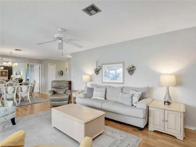 Living room featuring light wood-type flooring, a ceiling fan, a chandelier, and a textured ceiling