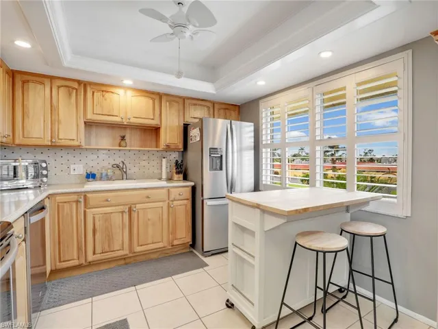 Kitchen with stainless steel appliances, open shelves, a tray ceiling, light countertops, and backsplash