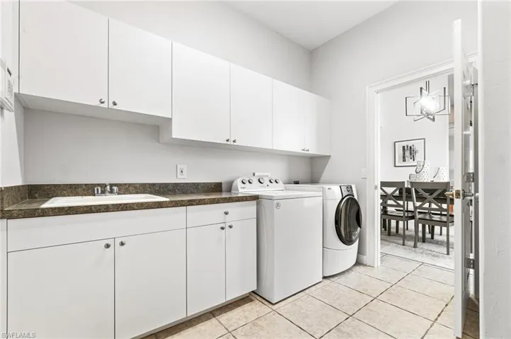 Laundry area featuring sink, cabinets, light tile floors, and washing machine and dryer