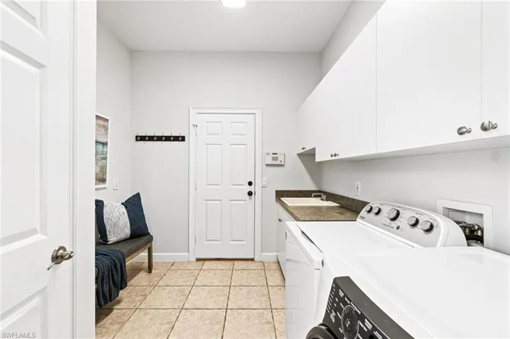 Clothes washing area featuring hookup for a washing machine, light tile floors, sink, washer and clothes dryer, and cabinets