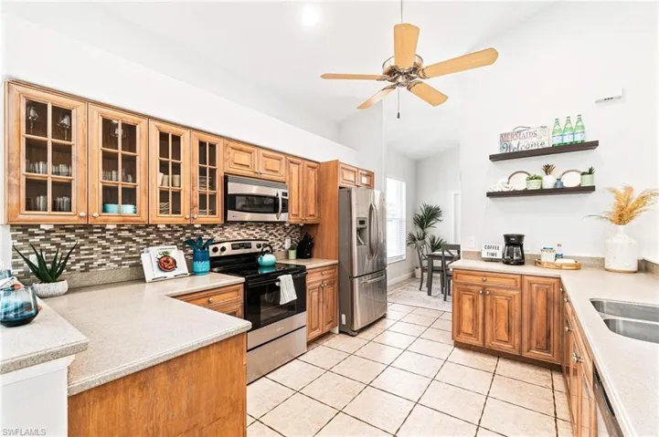 Kitchen featuring backsplash, ceiling fan, appliances with stainless steel finishes, light tile floors, and lofted ceiling