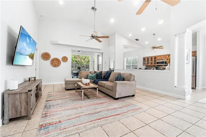Living room with high vaulted ceiling, ceiling fan, light tile flooring, and decorative columns