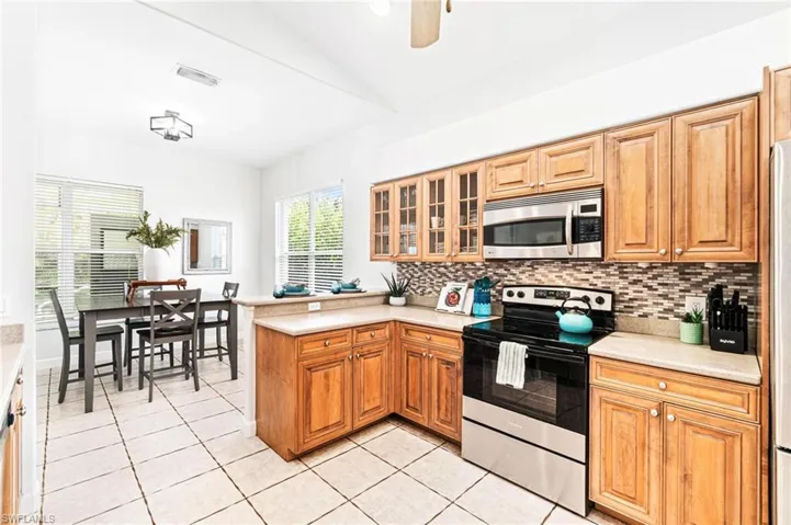 Kitchen with stainless steel appliances, light tile flooring, backsplash, and kitchen peninsula