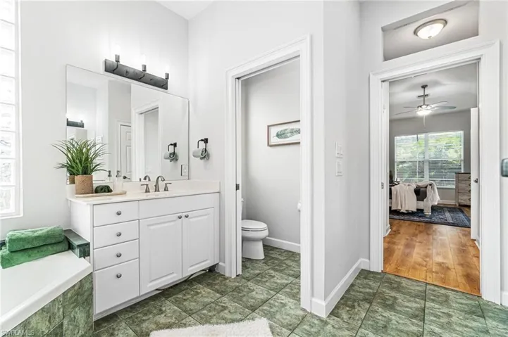 Bathroom featuring tiled tub, toilet, ceiling fan, tile flooring, and vanity