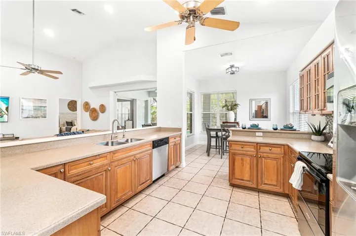 Kitchen with black electric range, ceiling fan, sink, light tile flooring, and dishwasher