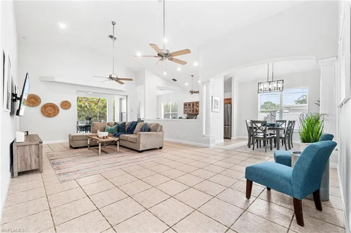 Living room with high vaulted ceiling, ceiling fan with notable chandelier, light tile floors, and decorative columns
