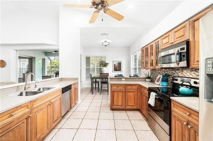 Kitchen with ceiling fan, stainless steel appliances, light tile flooring, backsplash, and sink