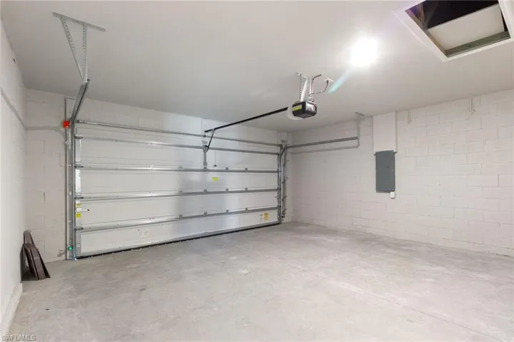 Garage with electric panel, concrete block wall, and a garage door opener
