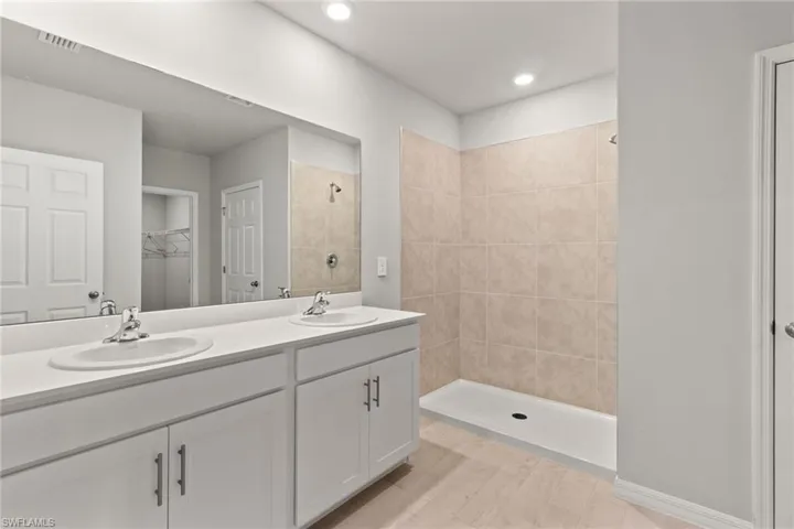 Bathroom with a spacious closet, double vanity, tiled shower, and recessed lighting
