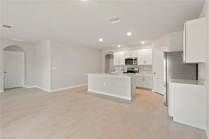 Kitchen featuring arched walkways, stainless steel appliances, an island with sink, white cabinets, and open floor plan