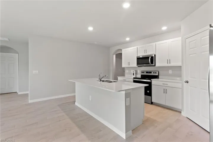 Kitchen with arched walkways, stainless steel appliances, a center island with sink, light wood-style flooring, and recessed lighting
