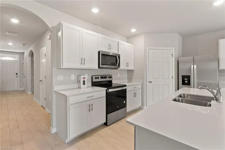 Kitchen with stainless steel appliances, arched walkways, white cabinets, light wood-style flooring, and recessed lighting